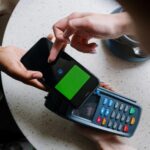 A close-up of a smartphone making a contactless payment on a terminal in a cafe setting.