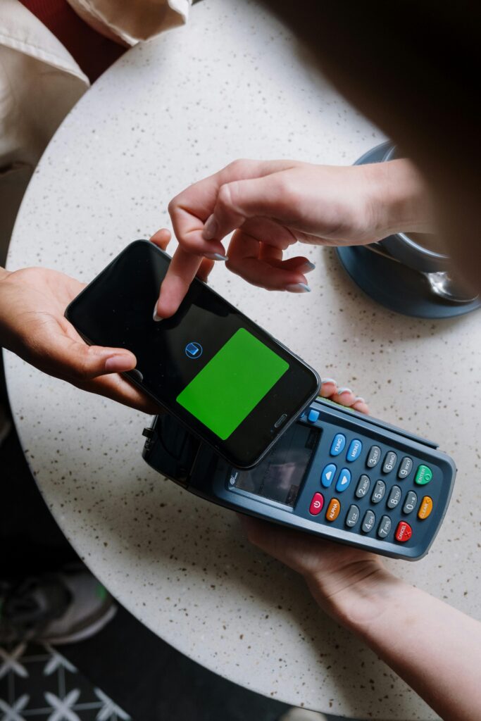 A close-up of a smartphone making a contactless payment on a terminal in a cafe setting.