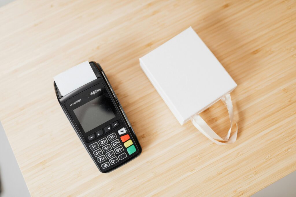 A payment terminal and a small white gift bag on a wooden countertop, ideal for commerce themes.